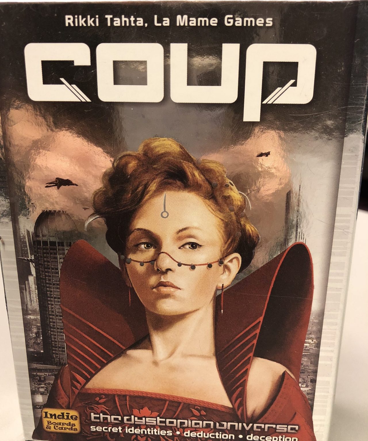 The front of the game box, which has a woman in a red dress with high shoulder pads standing in front of sky scrapers and looking very serious.